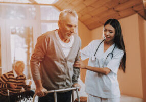 Doctor Supports Man. Pensioner on Go-Carts. Helps. Doctor Supports Man. Pensioner on Go-Carts. Caregiver. Adult Caucasian. Asian Nurse. Helps. Adult Walker. Nursing Home. Hard Go Himself. Nurse Hold. Old Bones. Chair Days. Retired. Medical Therapy.