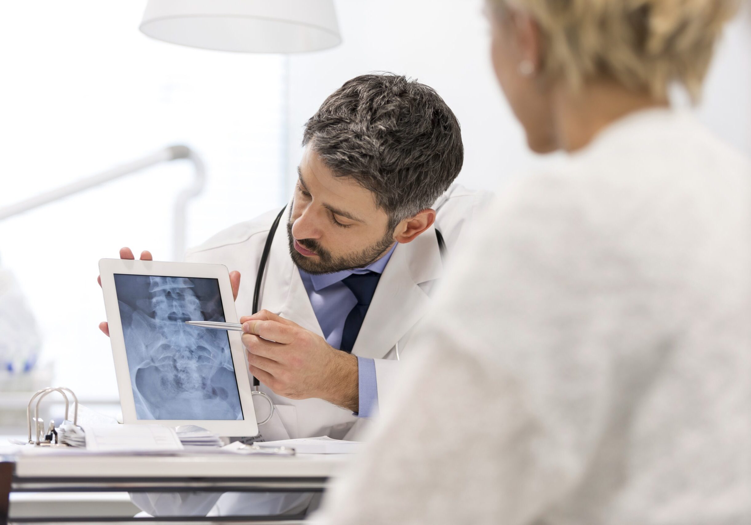 Doctor explaining x-ray on digital tablet to patient at desk in hospital